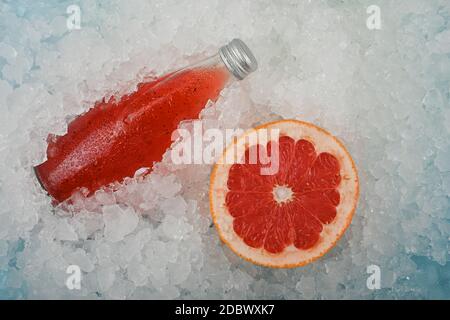 Nahaufnahme eine Glasflasche mit kaltem Saft-Cocktail-Getränk mit Chiasamen und halbgeschnittener rosa Grapefruit auf zerkleinertem Eis im Einzelhandel, erhöhter Hig Stockfoto