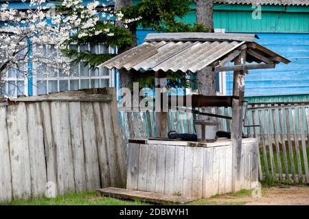 Öffentlicher lokaler alter Brunnen mit dem Eimer in einem russischen sterbenden Dorf im Frühling, Primorski kray, Russland Stockfoto
