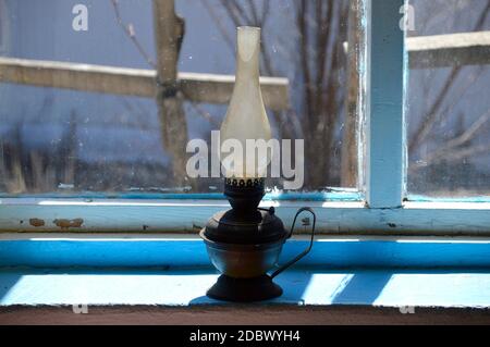 Gebrauchte Petroleumlampe mit flachem Docht (auch als Paraffinlampe bekannt) Auf alten schäbigen blauen Fensterbank im Sonnenlicht Stockfoto