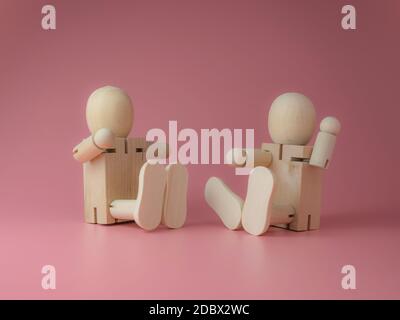 2 Holzpuppe sitzend und sprechende Gesten auf einem rosa Hintergrund. Konzept des sozialen Kontakts von Holzpuppen. Stockfoto