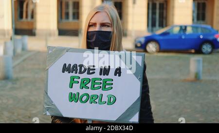 Made in a free world - Slogan auf Protestaktionen in der Stadt. Junge blonde Frau in Schutzmaske zu Fuß mit Dampfer. Stockfoto