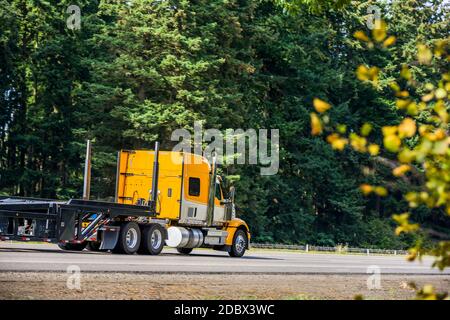 Leuchtend gelbe lange Schlepper großen Rig roten Industrie-semi-Truck Transport leerer Step Down Sattelauflieger läuft auf der Geraden autobahn Straße mit grün Stockfoto