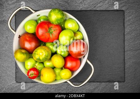 Grüne und rote Tomaten im Emailliersieb auf Schiefer Scheibe mit Kopierbereich Stockfoto