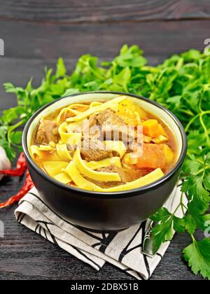 Zentralasiatisches Nationalgericht Lagenfleisch aus Fleisch, Nudeln und Gemüse in einer Schüssel auf einer Serviette, Knoblauch, Petersilie auf dunklem Holzbrett Stockfoto