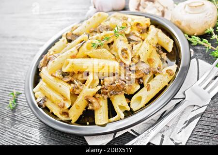 Penne Pasta mit Pilzen in einem Teller auf einem Küchentuch, Thymian, Gabel und Knoblauch auf Holzbrett Hintergrund Stockfoto