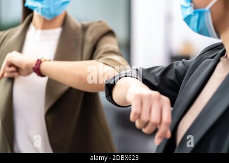 Nahaufnahme zwei Geschäftsfrauen tun alternative Begrüßung in neuen normalen Büroleben. Sie tragen eine schützende Gesichtsmaske und verwenden Ellenbogen-Beule anstelle von Handschal Stockfoto