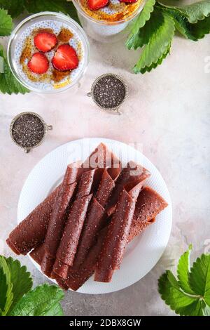 Erdbeer-Pastille auf einem weißen Teller und Chia-Samenpudding. Die Marshmallow wird in ein Rohr gerollt. Chia-Samen in Vintage-Gerichten. Speicherplatz kopieren. Vertikal Stockfoto