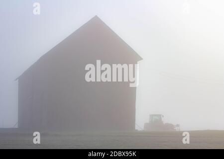 Nebel bedeckt einen deutschen schrägen Stall aus dem 19. Jahrhundert mit der Größe eines Feldtraktors daneben in den usa Stockfoto