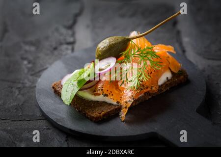 Lachs offenes Sandwich auf Pumpernickelbrot mit Gemüse, Kräutern und Weichkäse Stockfoto