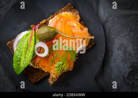 Lachs offenes Sandwich auf Pumpernickelbrot mit Gemüse, Kräutern und Weichkäse Stockfoto