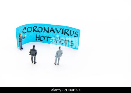 Präsentationstreffen mit Miniaturfiguren, die als Geschäftsleute stehen Vor der Post-it-Notiz mit Coronavirus Hotspots handgeschriebene Nachricht Stockfoto
