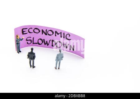 Präsentationstreffen mit Miniaturfiguren, die als Geschäftsleute stehen Vor dem Post-it-Hinweis mit Wirtschaftsverlangsamung handschriftliche Nachricht Zoll Stockfoto
