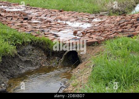 Ablaufleitung für Regenwasser, das in einem Graben läuft. Ein Ziegelstein geht durch sie hindurch. Russische Landschaft Stockfoto