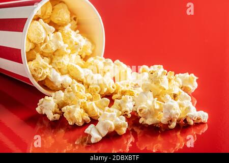 Süßes Popcorn im gestreiften Pappbecher auf rotem Hintergrund. Stockfoto