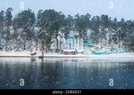 Leere Wasserrutsche mit Red Beach Hut in der Nähe des zugefrorenen See an einem kalten Wintertag mit Schnee in Wolken. Schweden Stockfoto