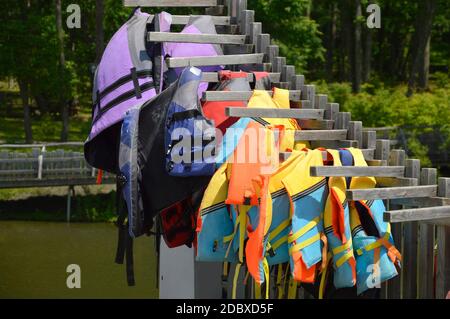 Viele bunte Schwimmwesten hängen auf einem hölzernen Stand in der Nähe Das Wasser Stockfoto