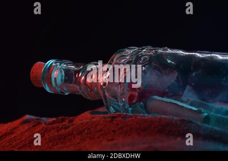 Nahaufnahme einer Nachricht in einer Flasche, die während des Nachtlichts an der sandigen Küste sichtbar ist. Stockfoto