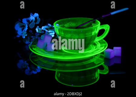 Eine glühende Uran Glas Teetasse und Untertasse unter etwas ultraviolettem Licht, um seine einzigartigen Eigenschaften zu zeigen. Stockfoto