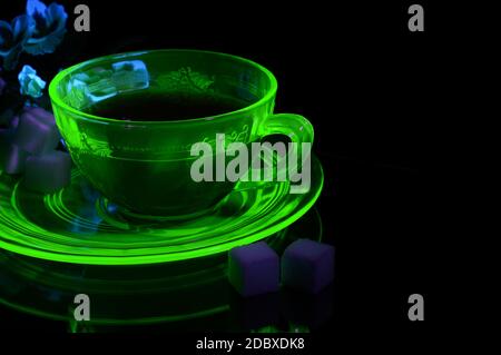 Eine glühende Uran Glas Teetasse und Untertasse unter etwas ultraviolettem Licht, um seine einzigartigen Eigenschaften zu zeigen. Stockfoto