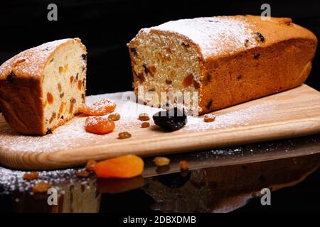 Süßer Cupcake in Form von Brot. Cupcake mit Rosinen, getrockneten Aprikosen, Pflaumen. Brot - Cupcake auf einem Holzbrett auf schwarzem Hintergrund, bestreut w Stockfoto