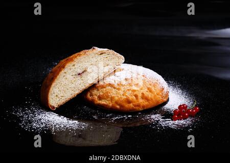 Süßer Cupcake in runder Brotform mit Füllung. Brot - Cupcake auf schwarzem Hintergrund, mit Pulver bestreut, mit Johannisbeeren verziert. Foto in secti Stockfoto