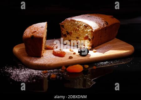 Süßer Cupcake in Form von Brot. Cupcake mit Rosinen, getrockneten Aprikosen, Pflaumen. Brot - Cupcake auf einem Holzbrett auf schwarzem Hintergrund, bestreut w Stockfoto