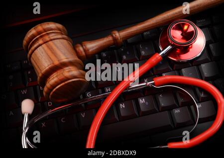 Eine Draufsicht auf einen legalen Holzgavel und Ärzte Stethoskop auf einem schwarzen Tastenfeld und einige rote Gelbeleuchtung, die die Szene auffällt. Stockfoto