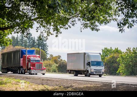 Zwei verschiedene Träger rot großen Rig semi-Truck mit trocken Transporter Sattelanhänger für Langstrecke und kleine Rig weiß Fahrerhaus über LKW mit Boxanhänger für lokale de Stockfoto