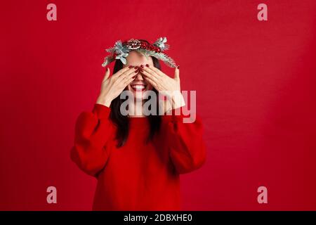 Nahaufnahme einer fröhlich lachenden asiatischen jungen Frau in einem Kranz, der ihre Augen mit den Händen bedeckt und auf ein Geschenk und ein neues Jahreswunder wartet, Stockfoto