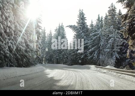 Blick von einem Auto reiten durch verschneite Winter Straße Kurve, beleuchtet durch die starke Sonne Hintergrundbeleuchtung - gefährliche Fahrsituationen. Stockfoto