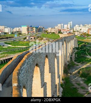 Historischer Anblick Kamares Aquädukt, Rasenplatz und Larnaca Stadtbild, bewölkte Skyline, Zypern Stockfoto