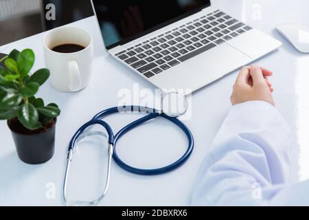 Mediziner arbeitet am Schreibtisch. Nahaufnahme des Stethoskops. Hand der asiatischen Frau Arzt erklären, um Patienten auf dem Tisch vor Laptop-Computer an der hos Stockfoto