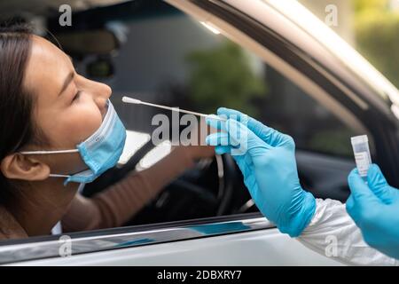 Portrait der asiatischen Frau Drive thru Coronavirus covid-19 Test durch medizinisches Personal mit PSA Anzug von Nase Tupfer. Neue normale Gesundheitsversorgung Drive-Thru-Service und Stockfoto