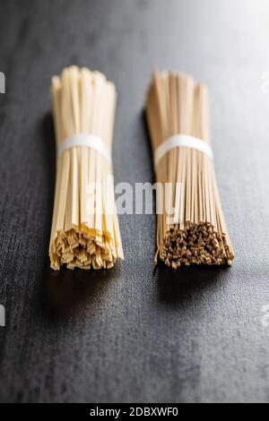 Ungekochte Soba- und udon-Nudeln. Traditionelle japanische Nudeln auf schwarzem Tisch. Stockfoto