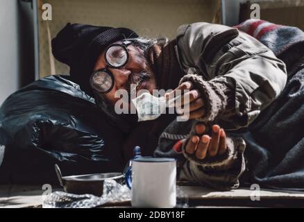 Der depressive Obdachlose bekommt von den Passanten Geldhilfe. Er ist arbeitslos und arbeitslos wegen der Coronavirus 19 Pandemie. Er lebt am Bürgersteig. Stockfoto