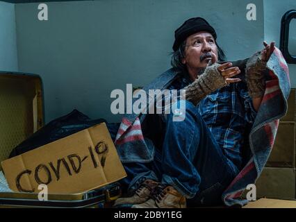 Ein arbeitsloser und obdachloser Mann bittet um Hilfe und Mitteilungan den Passanten, da er an einer Coronavirus-Pandemie leidet. Stockfoto