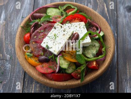 Hausgemachter griechischer Salat aus Tomaten, Gurken, Paprika, Käse, Oliven und Gemüse in einer Holzschüssel auf einem Holztisch. Gesundes, leckeres Essen Stockfoto