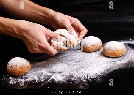 Hausgemachtes Gebäck. Weiße Brötchen werden von Hand getrennt. Foto des Backens auf schwarzem Hintergrund. Donuts mit Pulver bestreut. Stockfoto