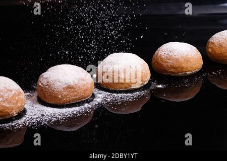 Backen auf schwarzem Hintergrund. Weiße Brötchen mit Pulver und Mehl bestreut. Backen zu Hause mit Pulver bestreut. Stockfoto