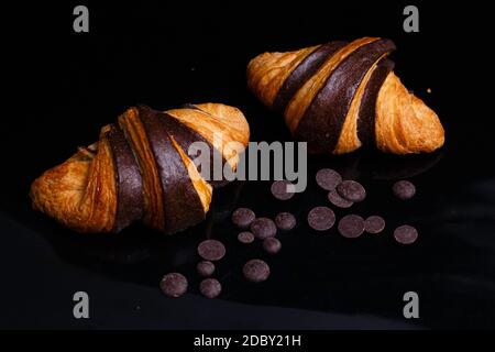Croissants mit Schokolade. Hausgemachtes Gebäck, Croissants mit Schokolade und Rosinen aus Schokolade. Foto von Croissants auf schwarzem Hintergrund Stockfoto