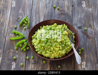 Kartoffelpüree mit grünen Erbsen und Olivenöl in einer Keramikschale auf einem Holztisch. Gesundes vegetarisches Essen Stockfoto