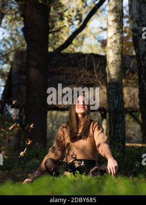 Junge schöne langhaarige Brünette Frau im Wald sitzen Mit herabfallenden Blättern Stockfoto