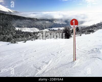 Red Ski route 1 Zeichen auf Neuschnee mit Schnee bedeckt Wald und Himmel im Hintergrund. Skigebiet Strbske Pleso, Slowakei Stockfoto