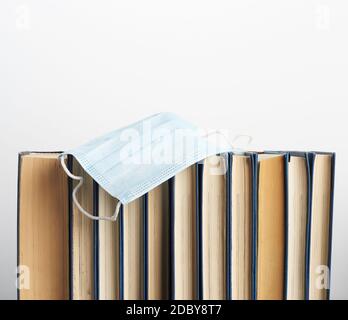 Stapel von verschiedenen Büchern und Einweg-medizinische Masken auf weißem Hintergrund, Konzept des Besuchs Bibliotheken in persönlichen Schutzausrüstung während quara Stockfoto