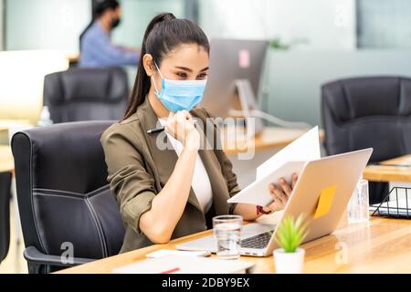 Asiatische Büro Mitarbeiter Geschäftsfrau tragen Schutzmaske Arbeit in Neue normale Büro mit interracial Business-Team im Hintergrund als Soziale Distanc Stockfoto