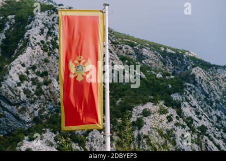 Rote Flagge Montenegros mit einem doppelköpfigen Adler vor einem Hintergrund von Bergen. Stockfoto