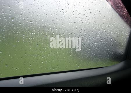 Verschwommene Regentropfen auf Fensterscheiben-Autoglas, Blick auf das neblige Spiegelauto mit Regentropfen Stockfoto
