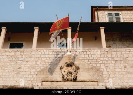 Flagge Montenegros über dem Haupttor in der Stadt Kotor auf einem Fahnenmast, in einem alten Backsteingebäude, in der Nähe eines Balkons mit Säulen. Stockfoto