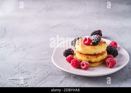 Quark Pfannkuchen und Puderzucker, Quark Fritters Dessert mit Himbeere und Brombeere Beeren in Teller auf Stein Beton Hintergrund Stockfoto