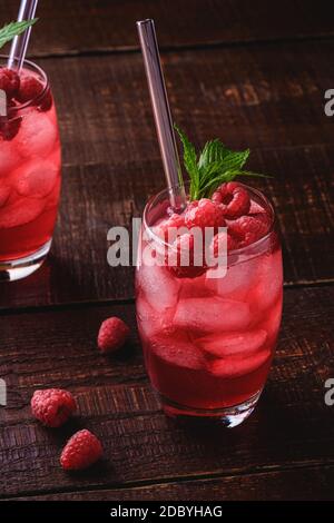 Frisch eiskalter Beerensaft Getränk mit Minze, Sommer Himbeer Limonade in zwei Glas mit Strohhalmen auf braunem Holzhintergrund, Winkelansicht selektiver Fokus Stockfoto